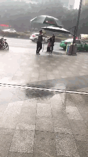 暖心!突降大雨 商场保安用遮阳伞为过街母女挡