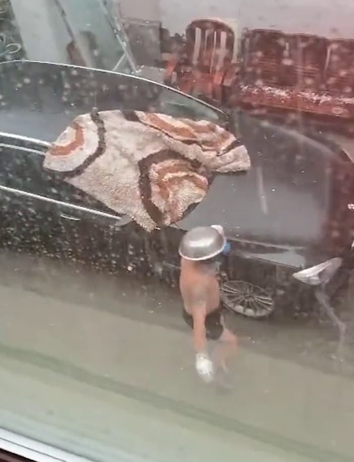 天降大雨冰雹 男子心疼爱车穿着短裤头顶钢盆拿毯子去盖车