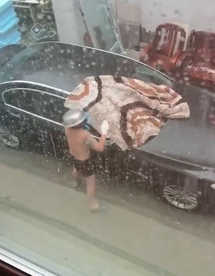 天降大雨冰雹 男子心疼爱车穿着短裤头顶钢盆拿毯子去盖车