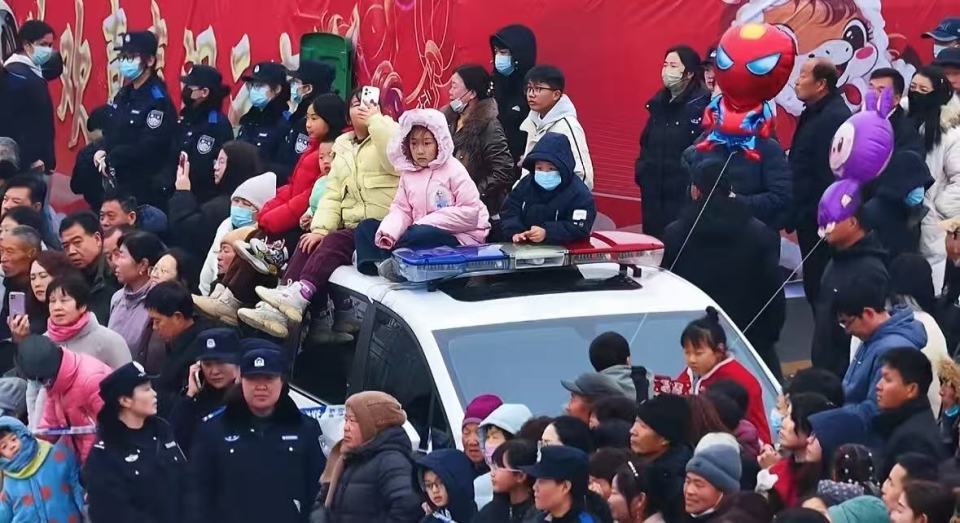 孩子们爬上警车观看表演，警员紧靠车辆牢牢守护